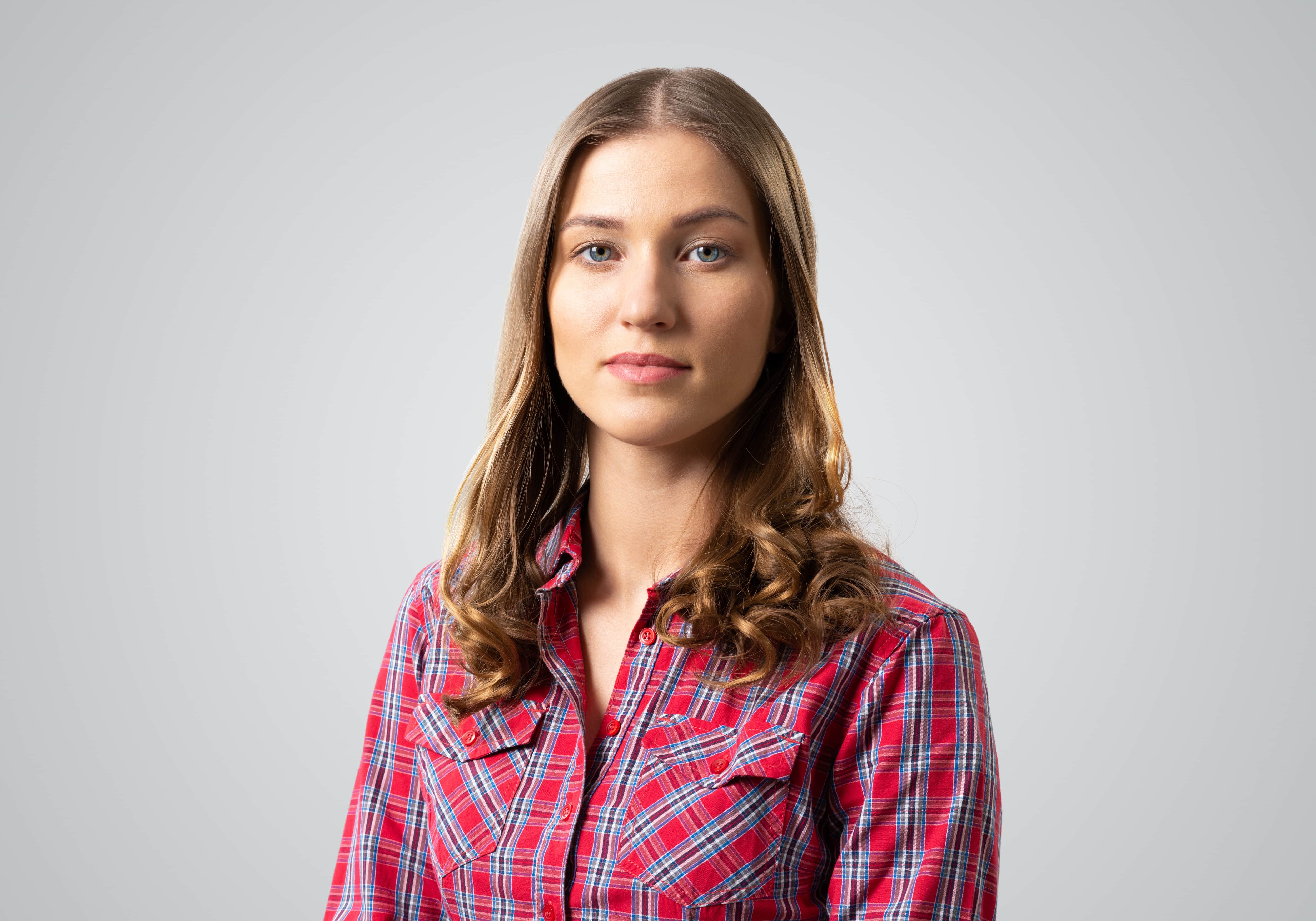 White woman wearing red plaid collared shirt looking straight into the camera with a neutral expression.